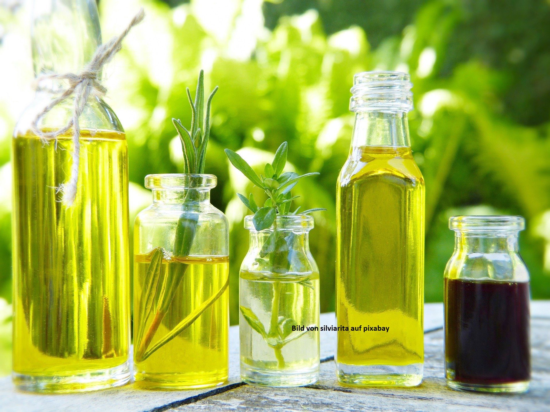 Verschiedene Öle in Glasflaschen nebeneinander, im Hintergrund Natur